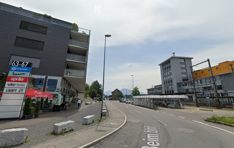An empty street with sidewalk, buildings, a sign, parked cars, and parked bicycles.
