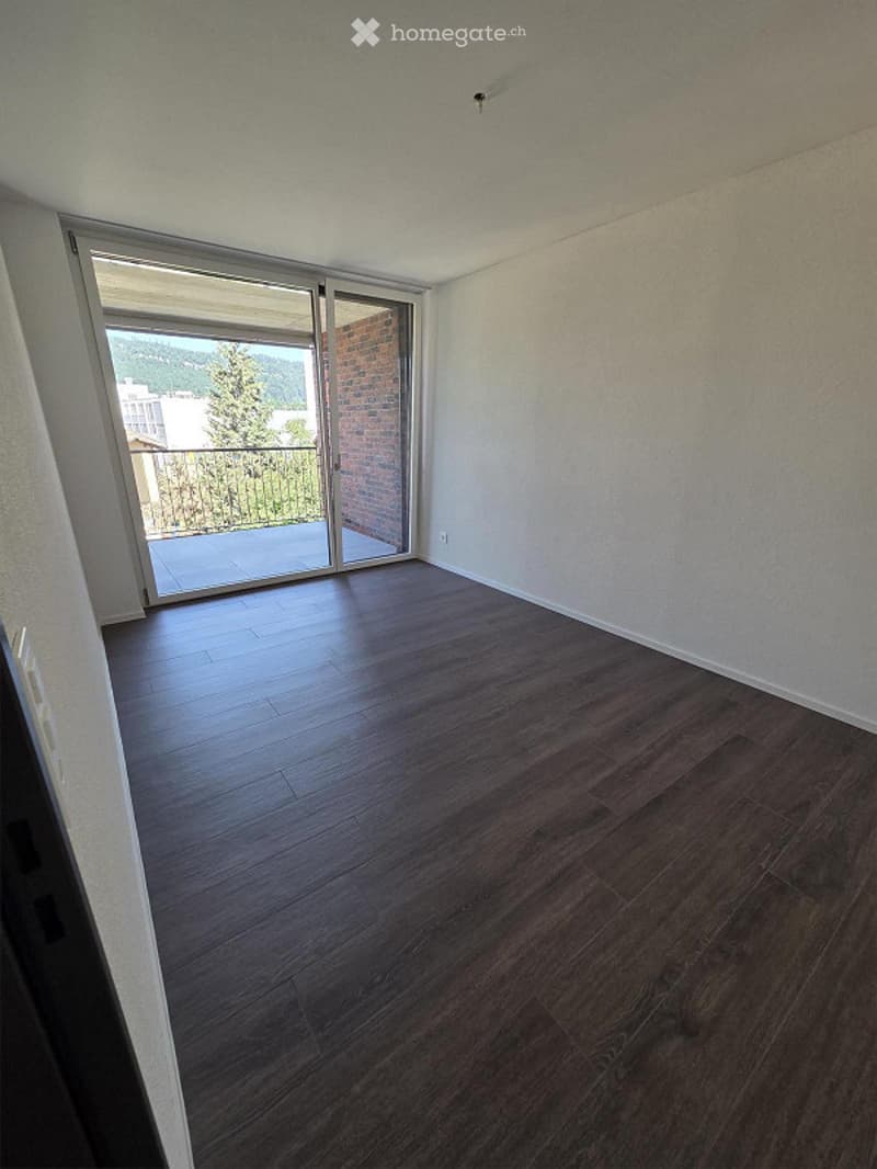 Empty room with dark wooden flooring, white walls, and large sliding glass doors leading to a balcony with a view.