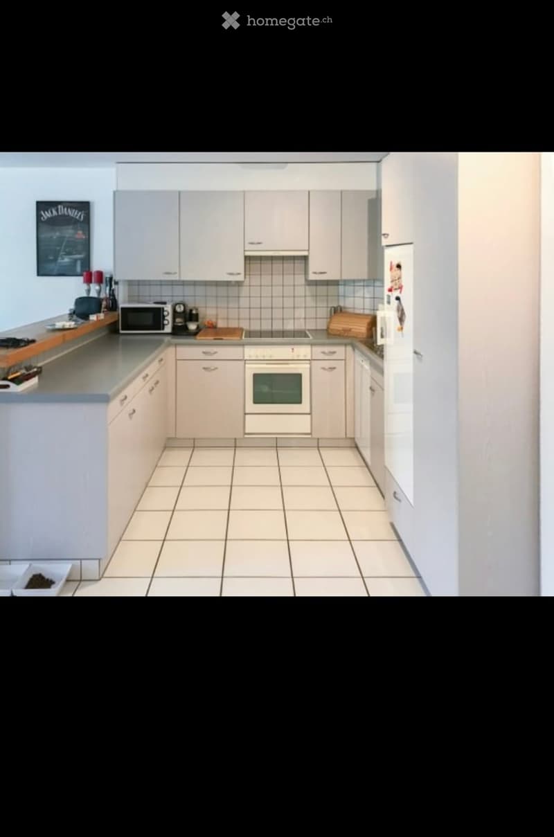 Modern kitchen with white cabinets, tiled floor, and stainless steel appliances including a microwave, oven, and refrigerator. Countertop features a cutting board and various small items.