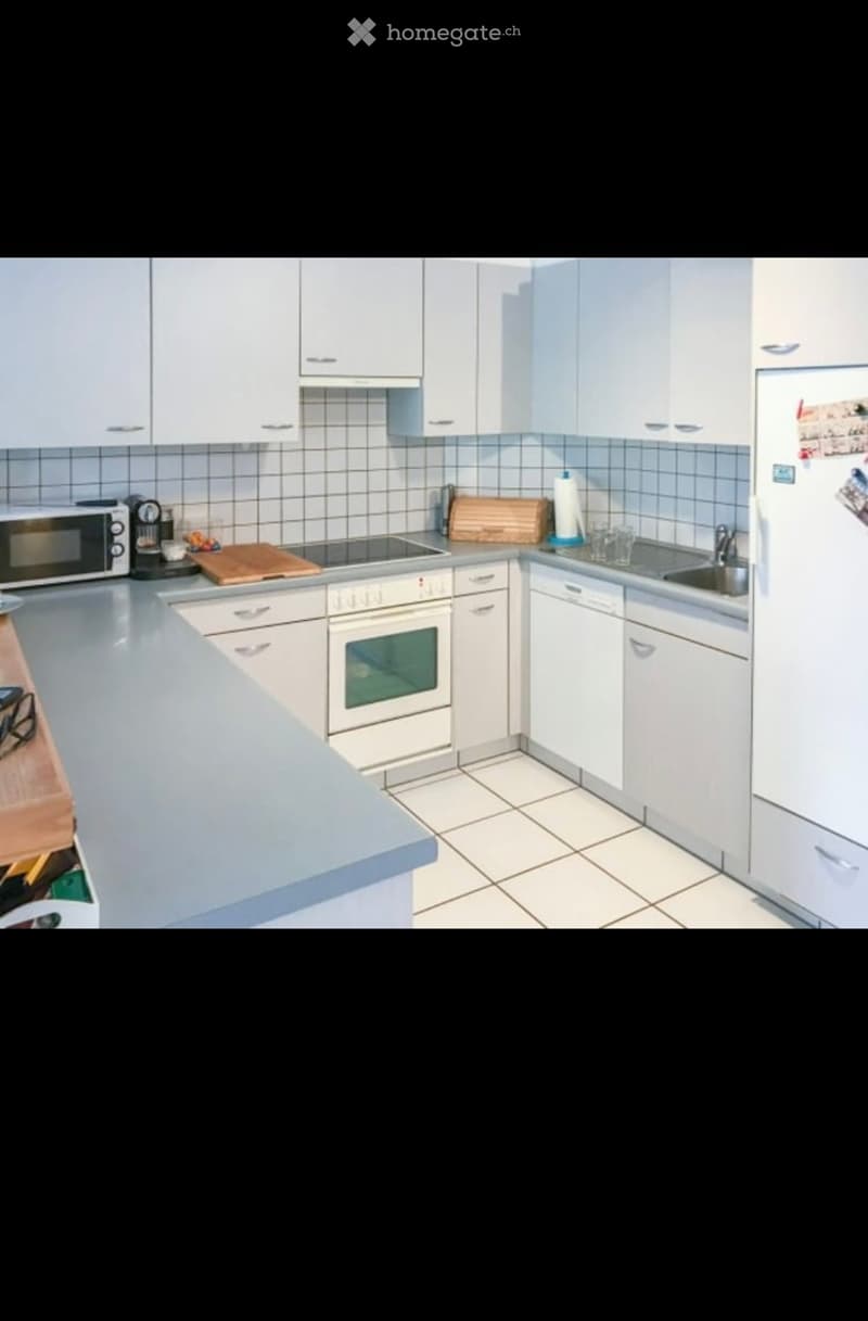 Modern kitchen with white cabinets, stainless steel appliances, and a light grey countertop. Features include a refrigerator, oven, microwave, sink, and dishwasher.