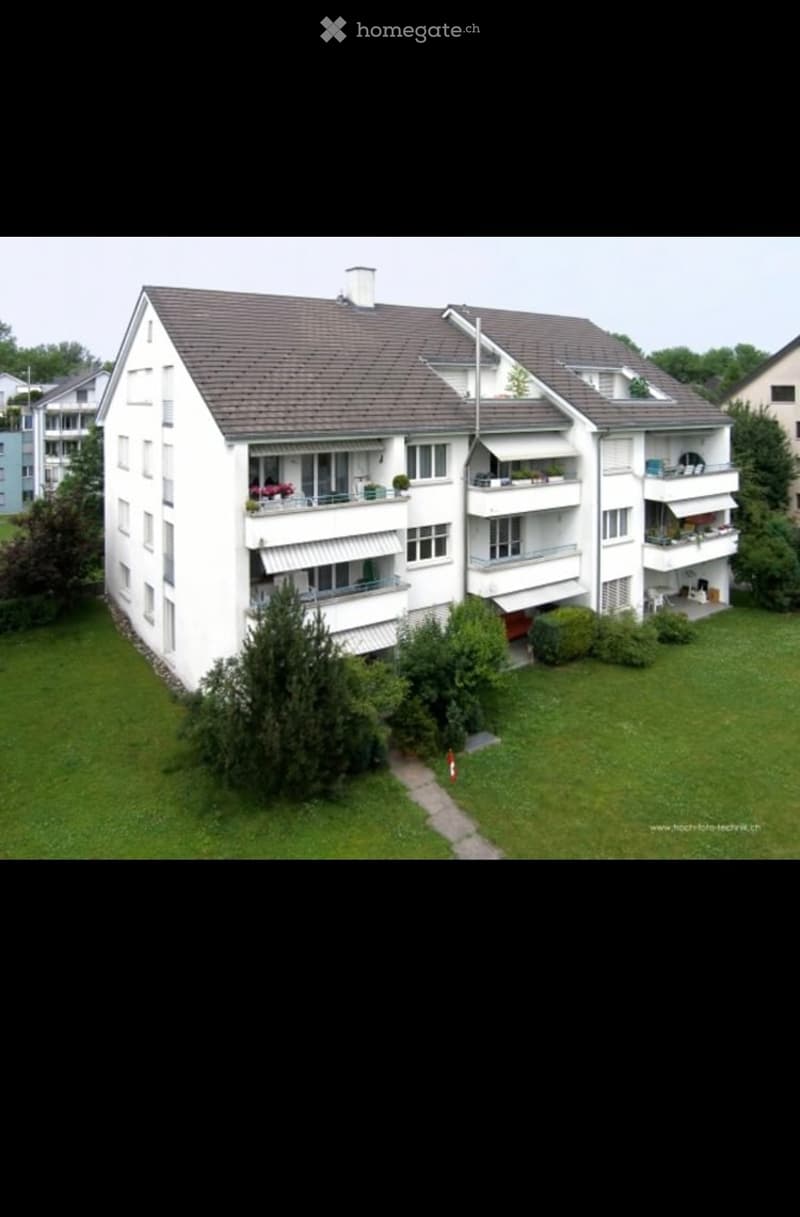 A multi-story residential building with multiple balconies, surrounded by greenery and a well-maintained lawn.