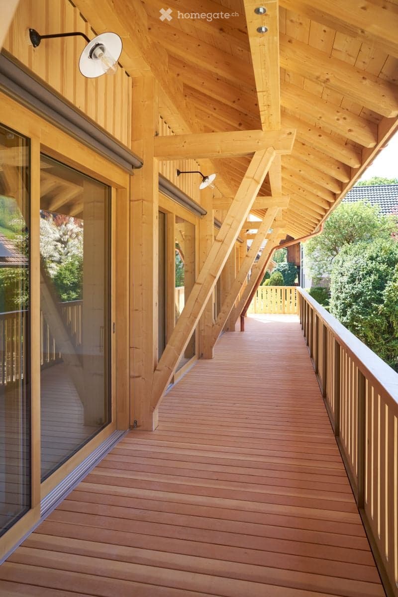 Wooden balcony with slatted flooring, wooden railings, and exposed wooden beams on the ceiling.