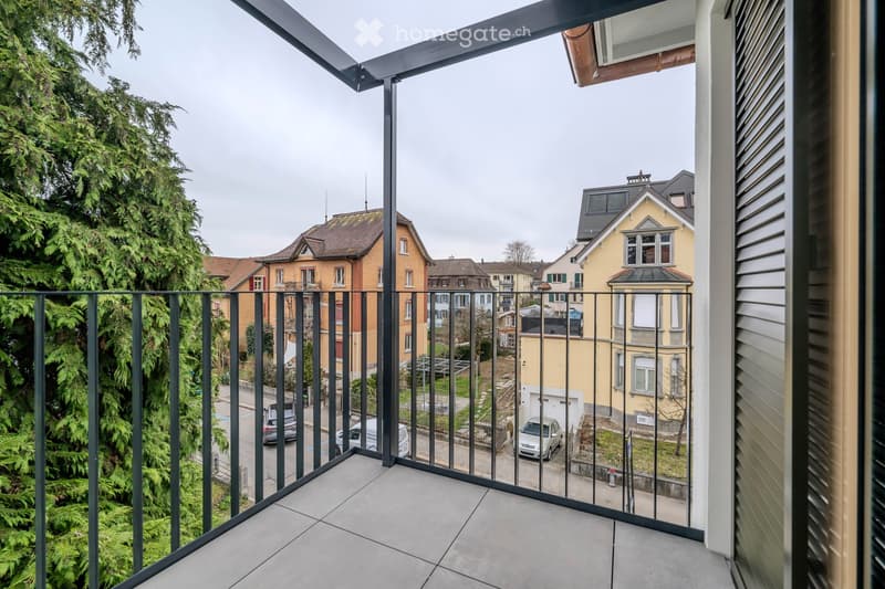 Balcony with metal railing, panoramic city view, several parked cars