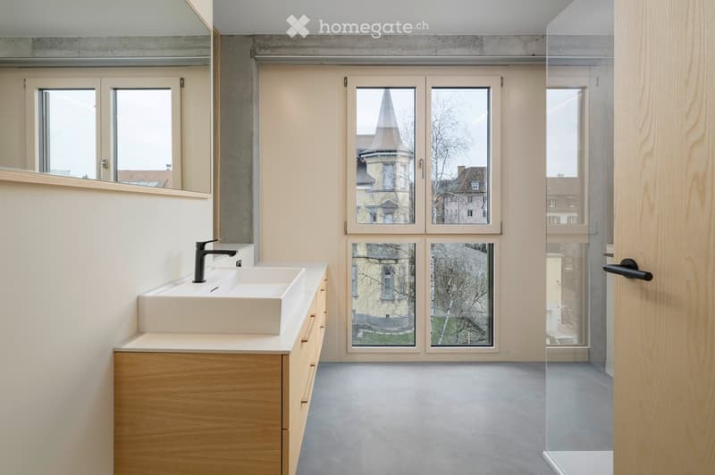 Modern bathroom with white sinks, gray floors, and large windows providing a view of the outside