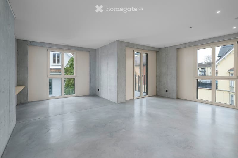 Empty room with concrete floors, large glass windows, beige walls, two shelves, open to the outdoors.
