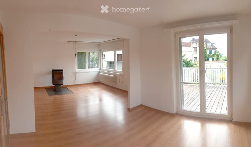 Empty room with wooden flooring, white walls, large windows, and a fireplace. No furniture or equipment present.