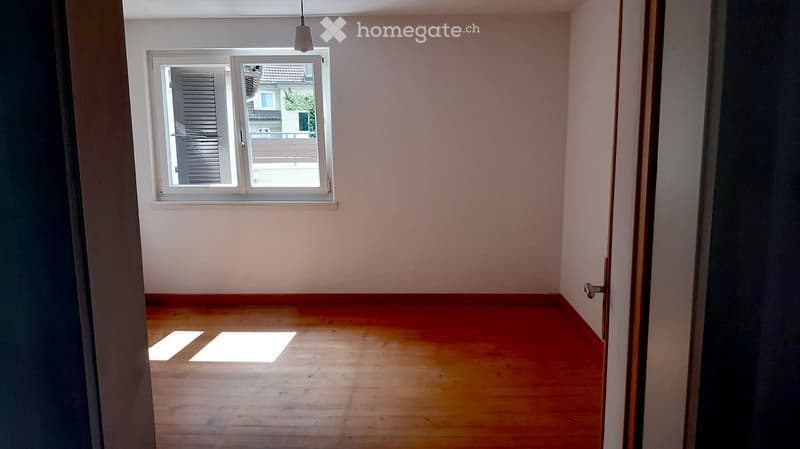 Empty room with wooden flooring and a window with blinds, allowing natural light to enter.