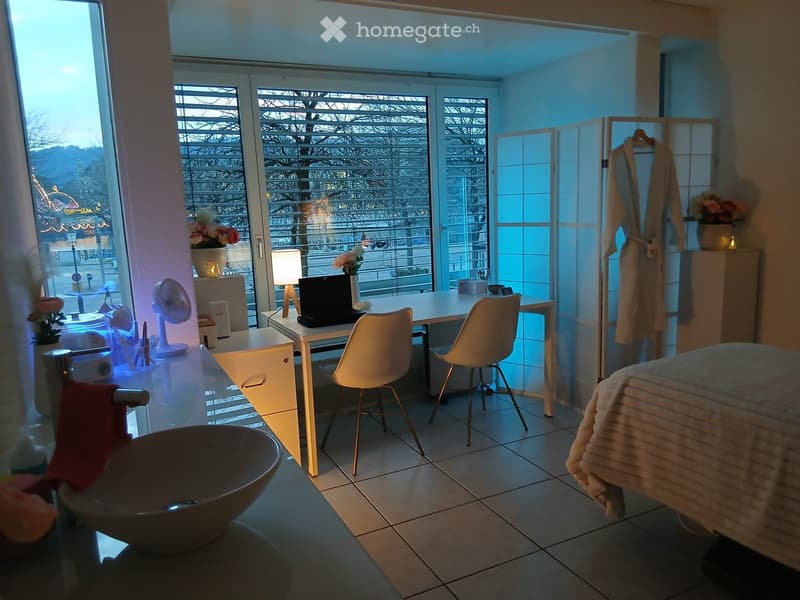 Well-lit room with a bed, desk, and chair, featuring a large window with a view, a fan, and decorative vases.