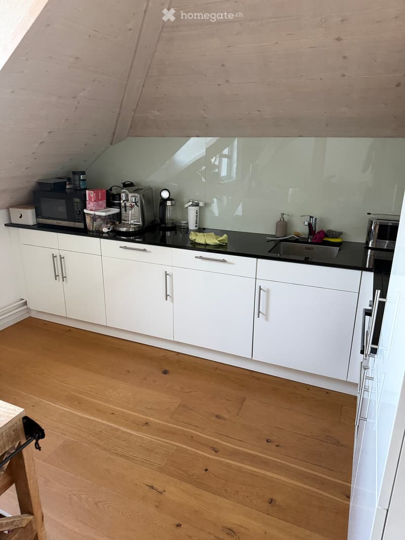 Modern kitchen with white cabinets, black countertops, and wooden flooring. Appliances include a microwave, coffee maker, and sink.