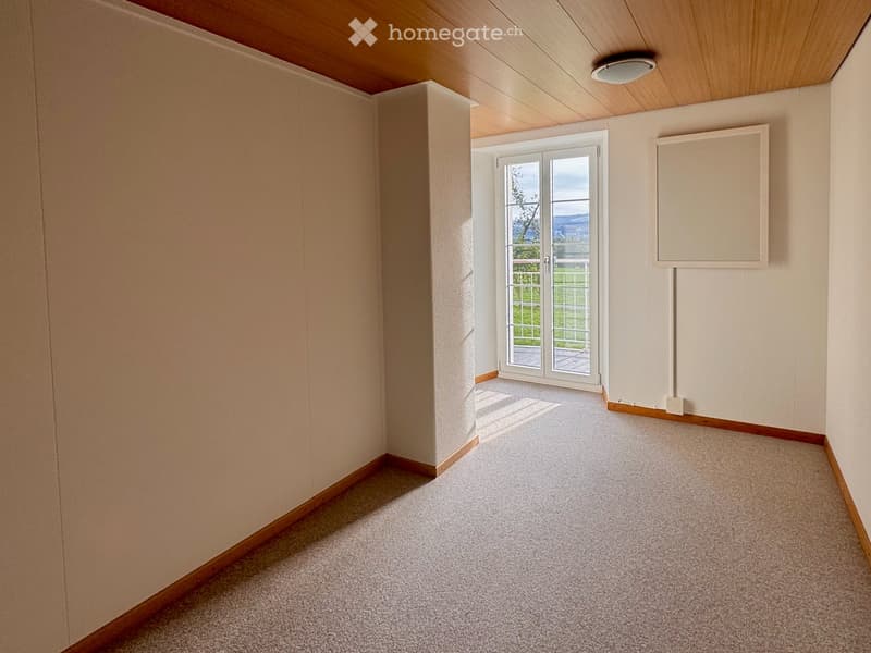Empty room with light-colored walls, carpeted floor, and a large window with a view of the outdoors.