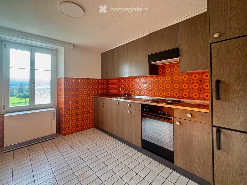 Modern kitchen with wooden cabinets, stainless steel appliances, and a retro orange backsplash. Features a sink, oven, and refrigerator.