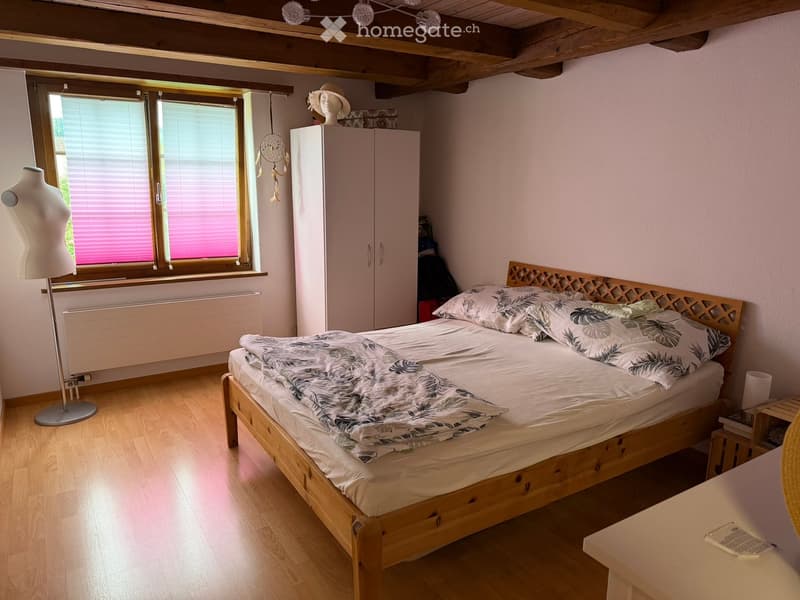 Cozy bedroom with wooden bed, matching nightstand, wardrobe, and mannequin near window with blinds.