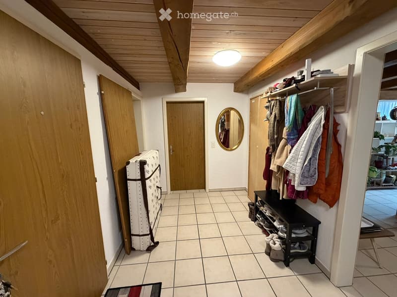 Hallway with tiled floor, wooden ceiling beams, coat rack, shoe rack, and a round mirror on the wall.