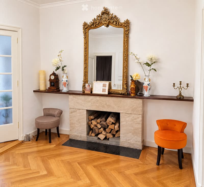Elegant living room with a stone fireplace, ornate mirror, two armchairs, decorative vases, and a candle holder on the mantel.