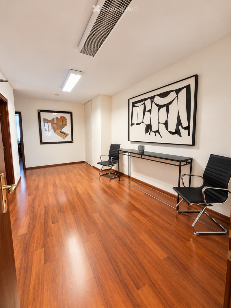 Modern, minimalist room with polished wooden flooring, two black chairs, a sleek black table, and two large framed artworks on the walls.