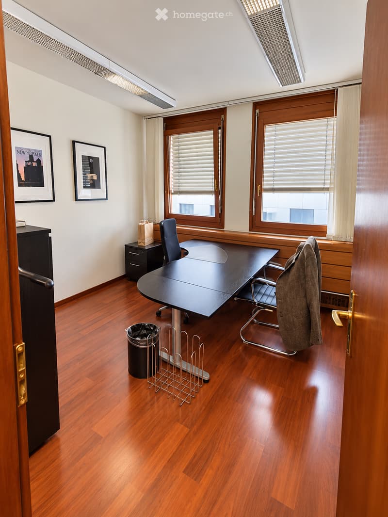 Office space with wooden flooring, large desk, office chairs, filing cabinet, trash can, magazine rack, and two picture frames on the wall.