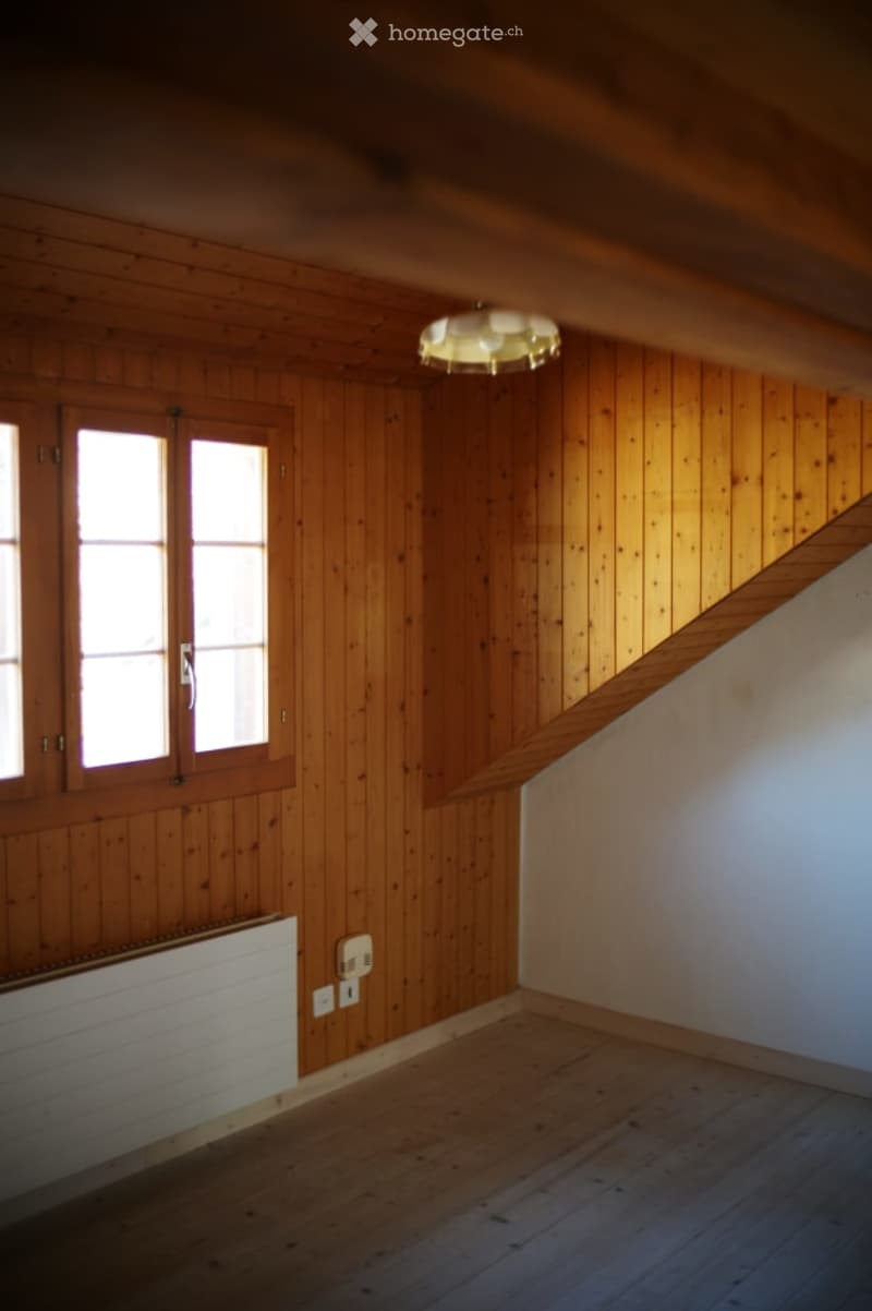 Empty room with wooden walls and floor, large windows, and a staircase leading upwards.