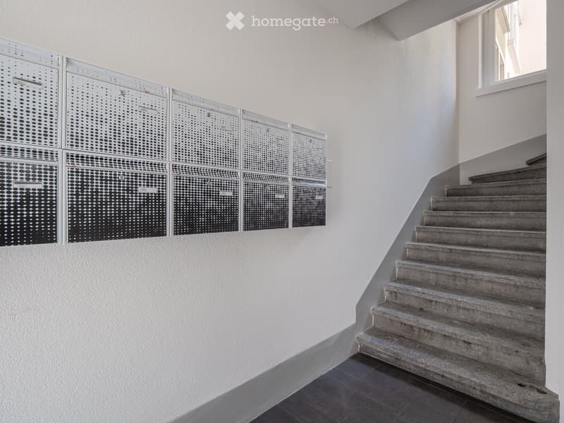 A modern hallway with a concrete staircase, white walls, and a decorative perforated metal panel on one side.