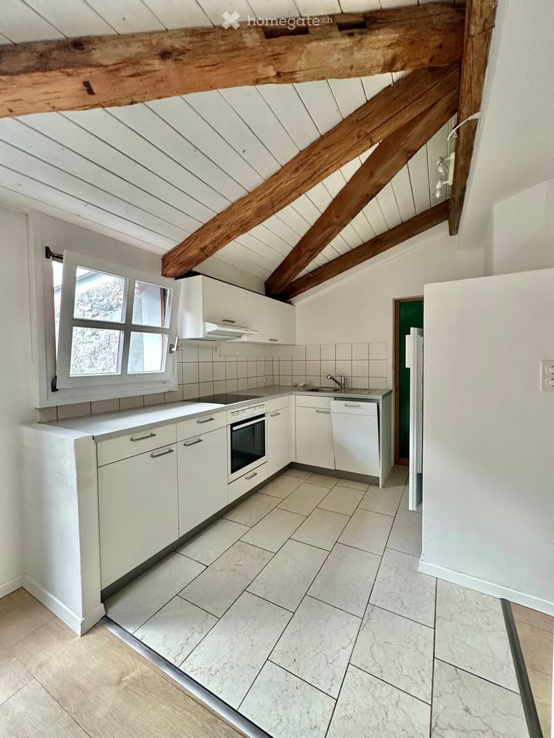 Modern kitchen with white cabinets, stainless steel appliances, and a marble tile floor. Features an exposed wooden ceiling beam and a window with multiple panes.