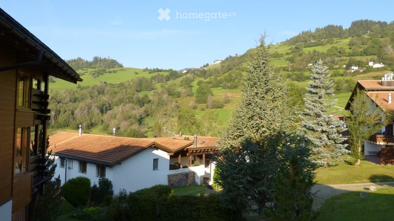 Scenic view of a rural village with houses, green hills, and trees under a clear blue sky.