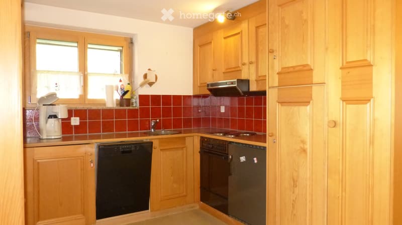 A well-lit kitchen with wooden cabinets, a coffee maker, dishwasher, oven, refrigerator, and a sink.