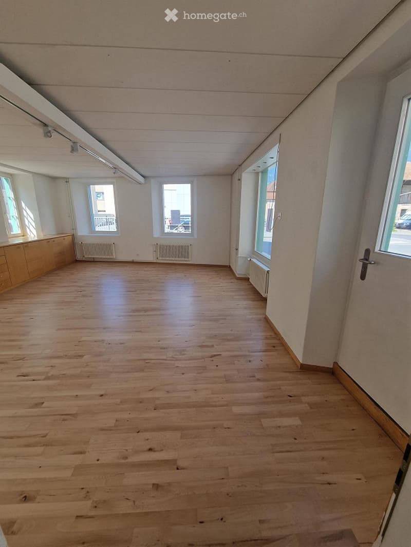 Empty room with wooden flooring, white walls, large windows, and built-in wooden cabinetry along one wall.