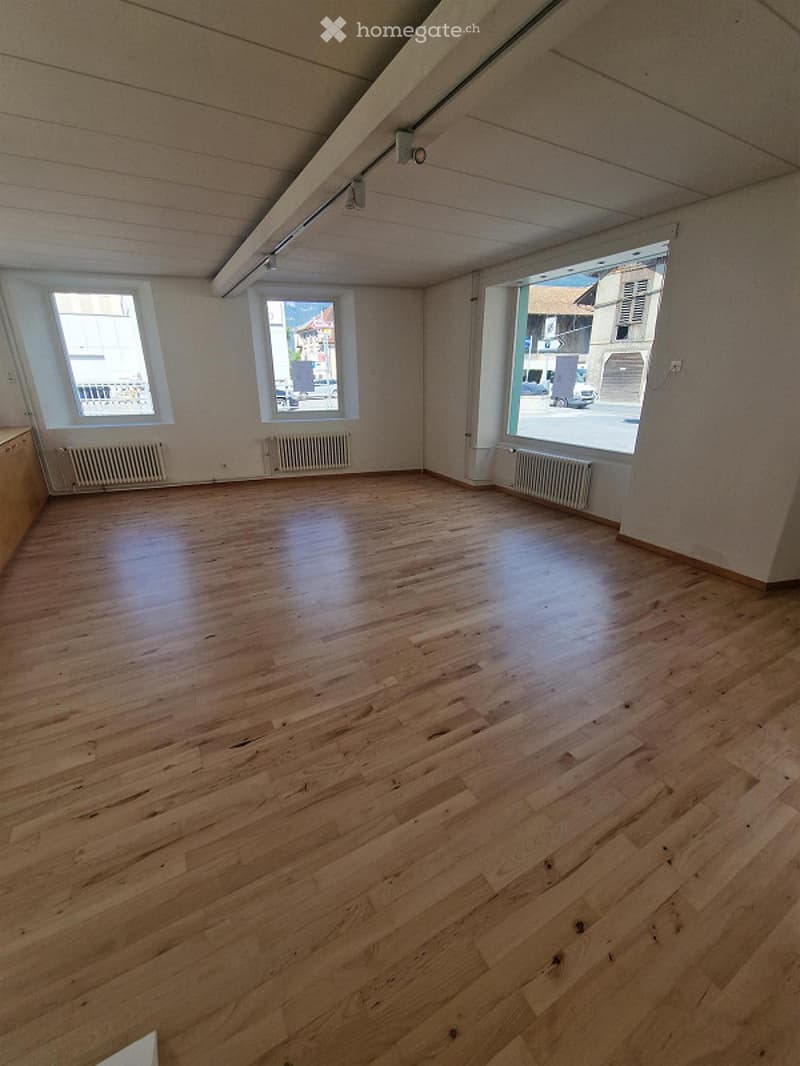 Completely empty room with wooden flooring, white walls, and large windows allowing natural light. No furniture or equipment present.