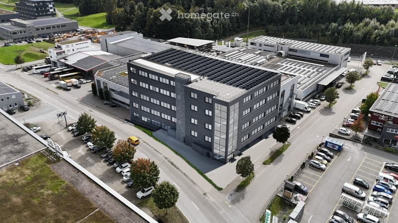 Aerial view of a modern industrial building complex with multiple structures, parking lots, and solar panels on the roofs.