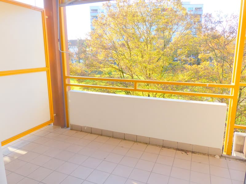 Balcony with tiled floor, white railing, and view of trees and buildings.
