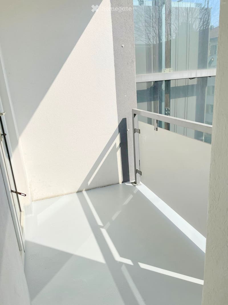 Modern balcony with white flooring, glass railing, and metal gate.