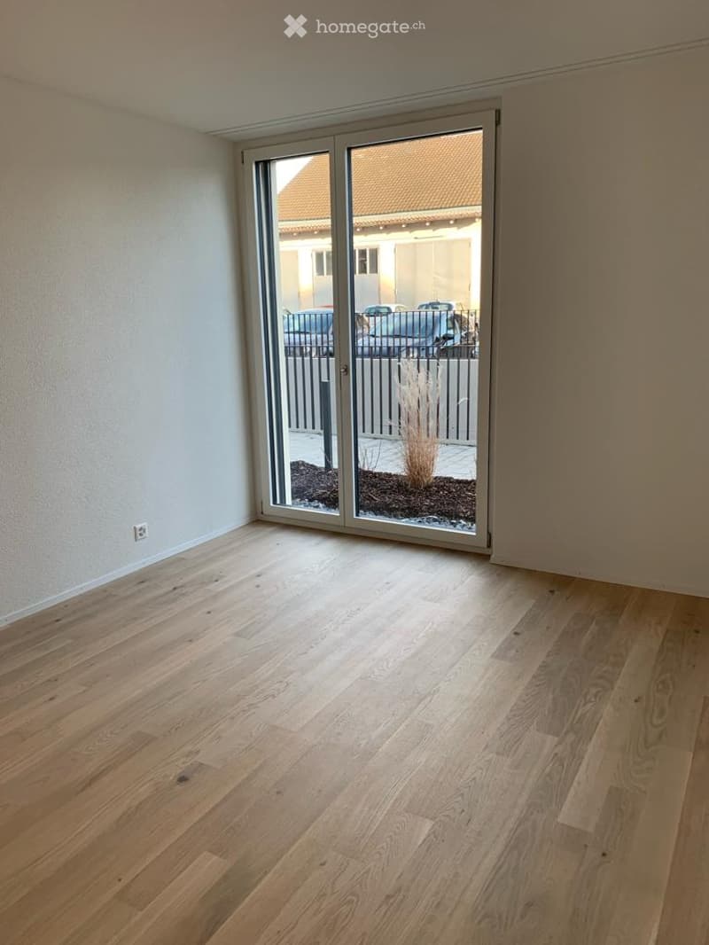 Empty room with light wooden flooring and large sliding glass doors leading to an outdoor area.