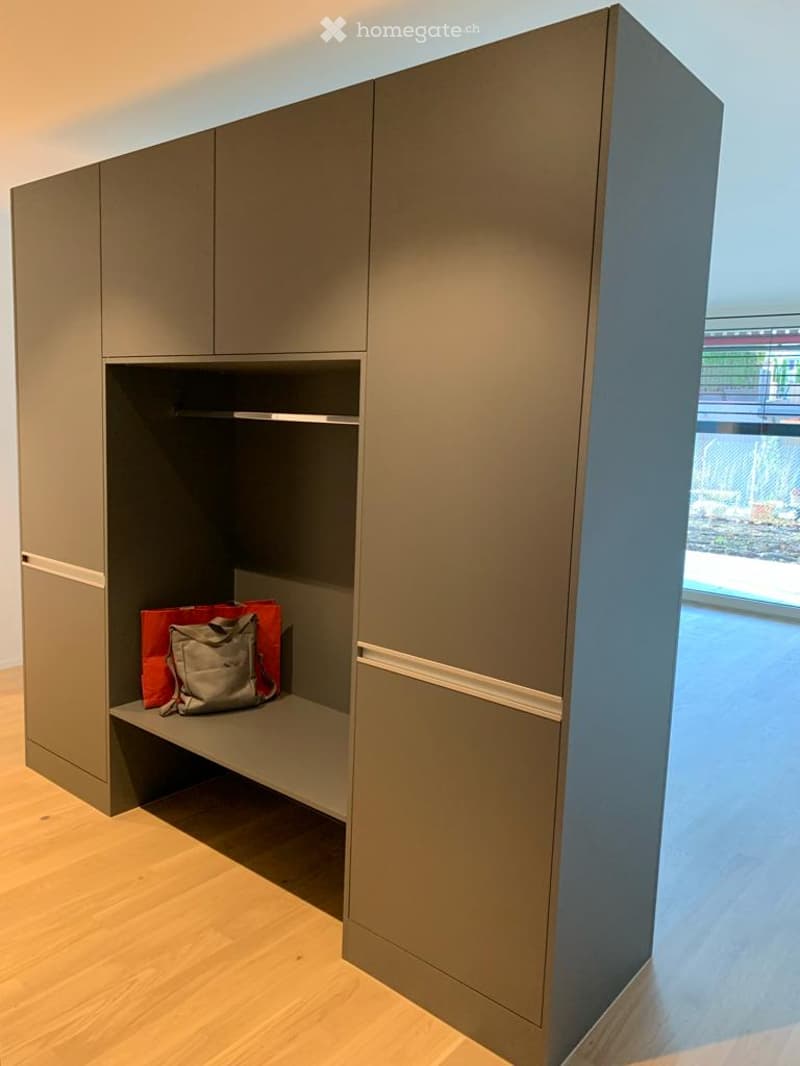 Modern grey wardrobe with built-in shelf and hanging space, containing a handbag and other items.