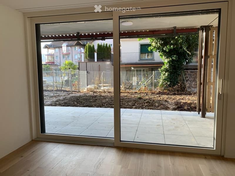 Large sliding glass doors open to a tiled balcony area with a view of a fenced yard and neighboring buildings.