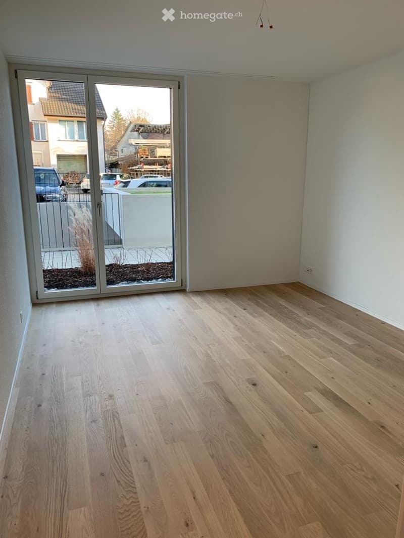 Empty room with light wooden flooring, white walls, and large glass sliding doors leading to an outdoor area.