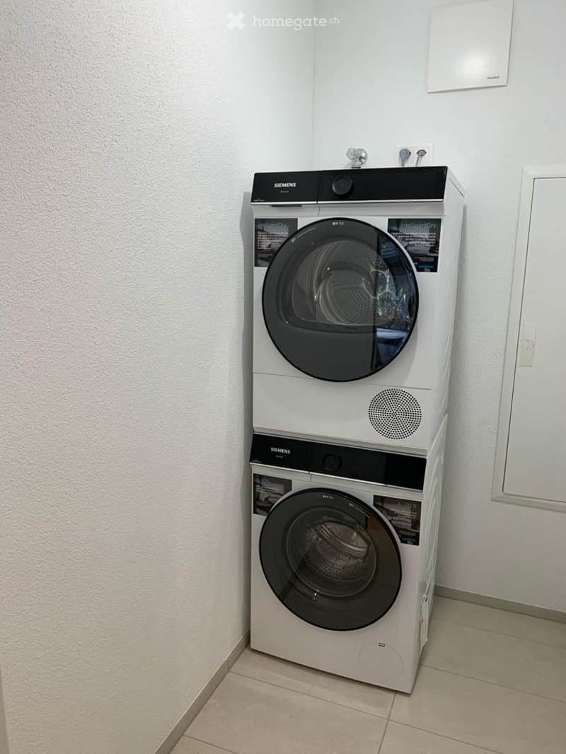 A modern bathroom featuring a stacked Siemens washing machine and dryer unit against a white wall.
