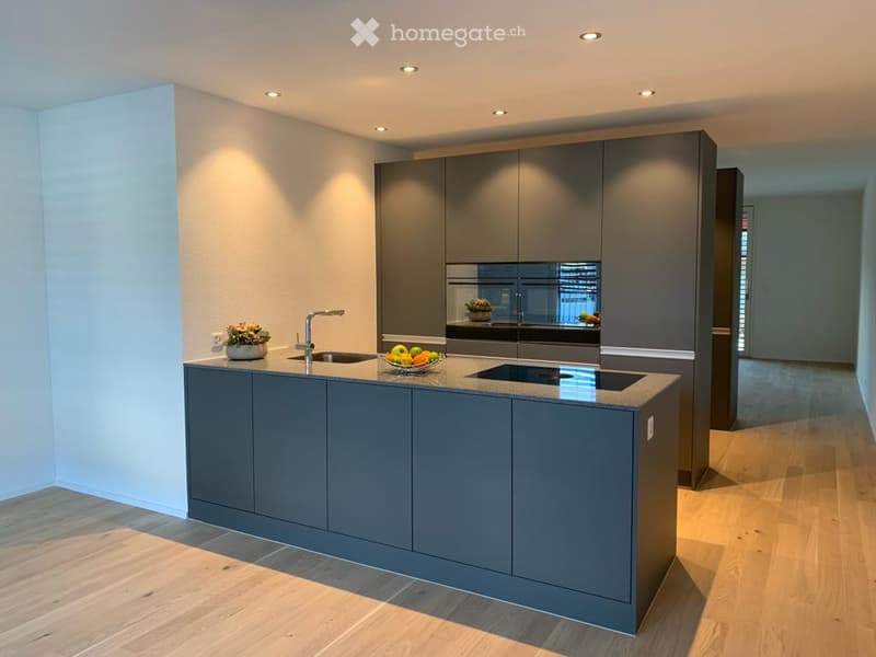 Modern kitchen with grey cabinets, a central island, an induction cooktop, a sink, and a fruit bowl on the counter.