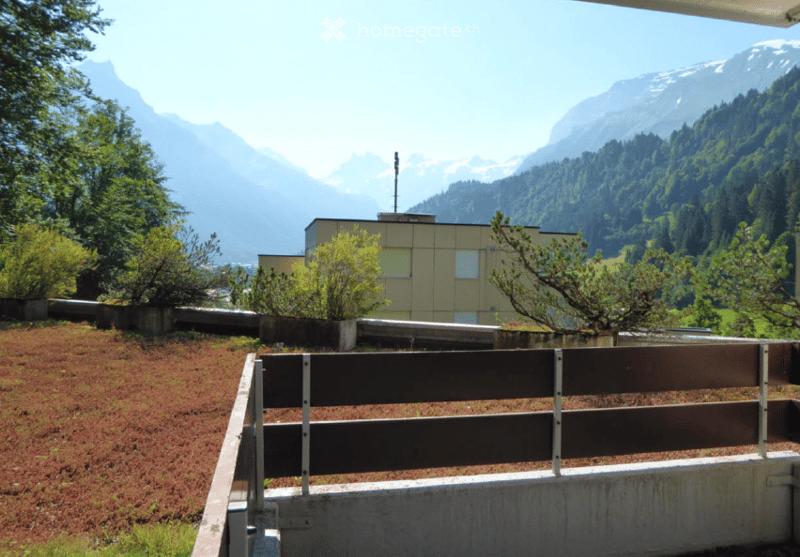 Exterior view of a building with mountains in the background, surrounded by greenery.