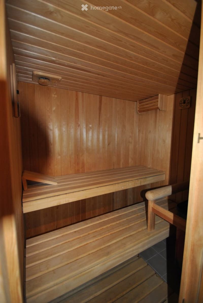 Wooden sauna with multiple wooden benches and a small control panel on the wall.