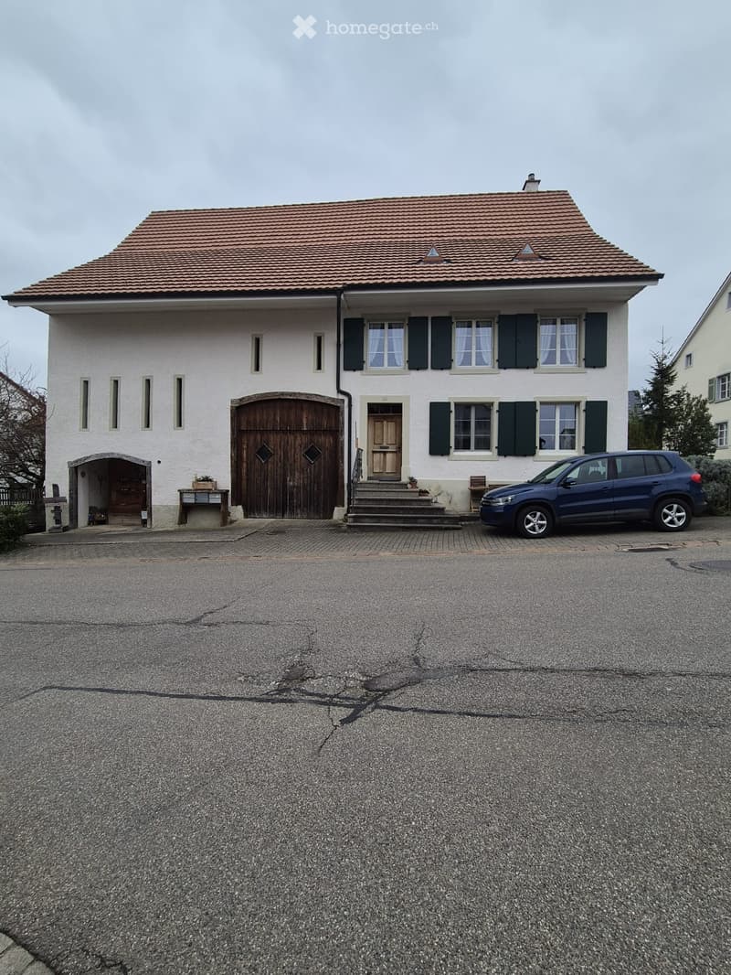 Two-story house with white walls, dark green shutters, a wooden garage door, and a blue SUV parked in front.