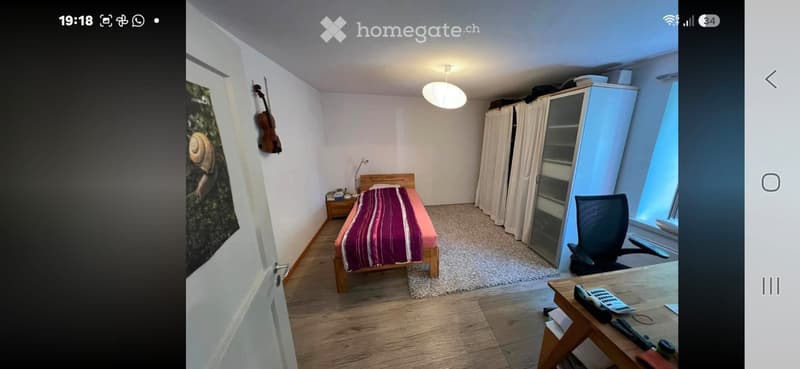 Cozy bedroom with a single bed, wooden chair, small table, large cabinet with curtains, and a guitar on the wall.