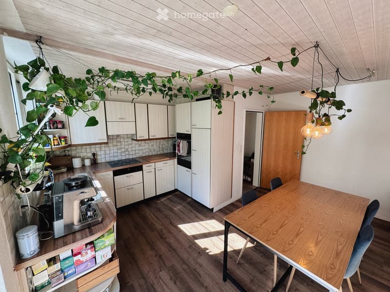 Modern kitchen with white cabinets, wooden countertops, and a dining area featuring a wooden table and chairs. Includes a coffee machine, dishwasher, and various kitchen appliances.