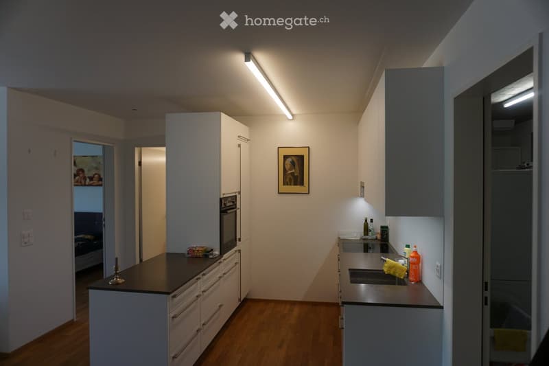 Modern kitchen with white cabinets, dark countertops, and built-in appliances. Features a sink, oven, and various kitchen items on the counter.