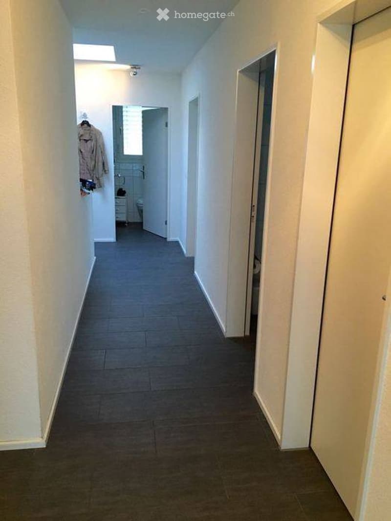 Empty hallway with tiled floor, white walls, and several doors leading to rooms.