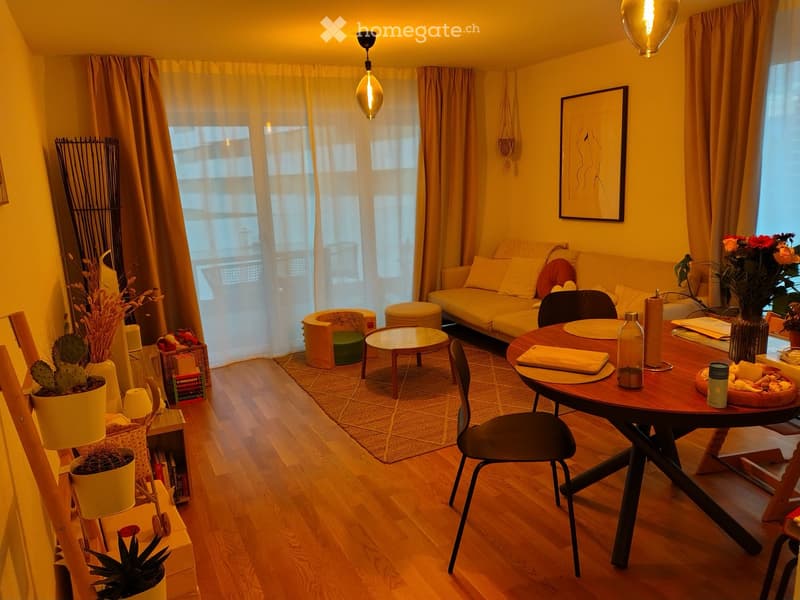 A cozy living room with wooden flooring, a sofa, coffee table, dining table, chairs, and decorative plants.