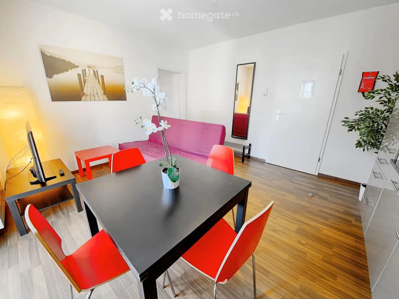 Modern living room with a black dining table, red chairs, a pink sofa, a TV, and a mirror on the wall.