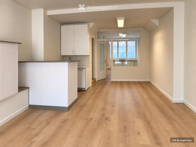 Empty room with wooden flooring, white walls, and a small kitchen area with cabinets and a dishwasher visible in the background.