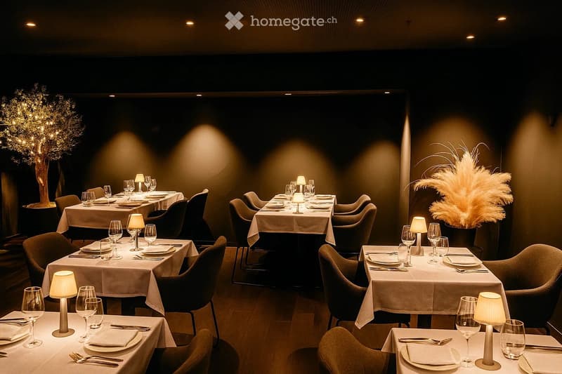 Elegant restaurant interior with multiple dining tables set with plates, wine glasses, cutlery, and napkins, surrounded by chairs and decorative lamps. The space features warm lighting and a sophisticated ambiance.