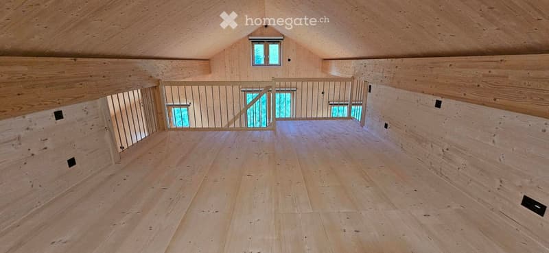 Empty attic space with wooden walls, ceiling, and floor, featuring a metal railing and windows.