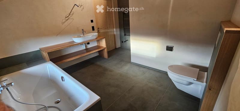 Modern bathroom with a bathtub, toilet, sink on a wooden shelf, and tiled floor.