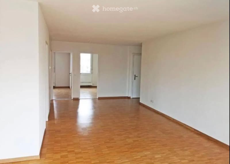 Empty hallway with wooden flooring and white walls, featuring several doors leading to other rooms.
